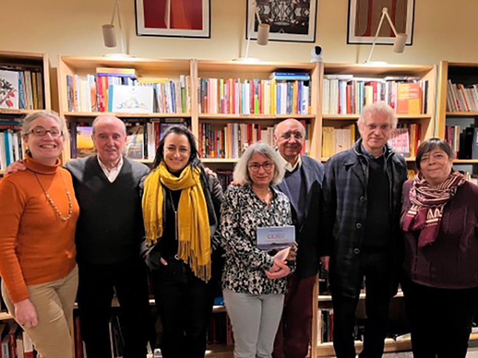 Grupo de sete pessoas em frente a estantes de livros na Livraria Portuguesa de Bruxelas, durante um evento literário dedicado à escultora Maria Leal da Costa.