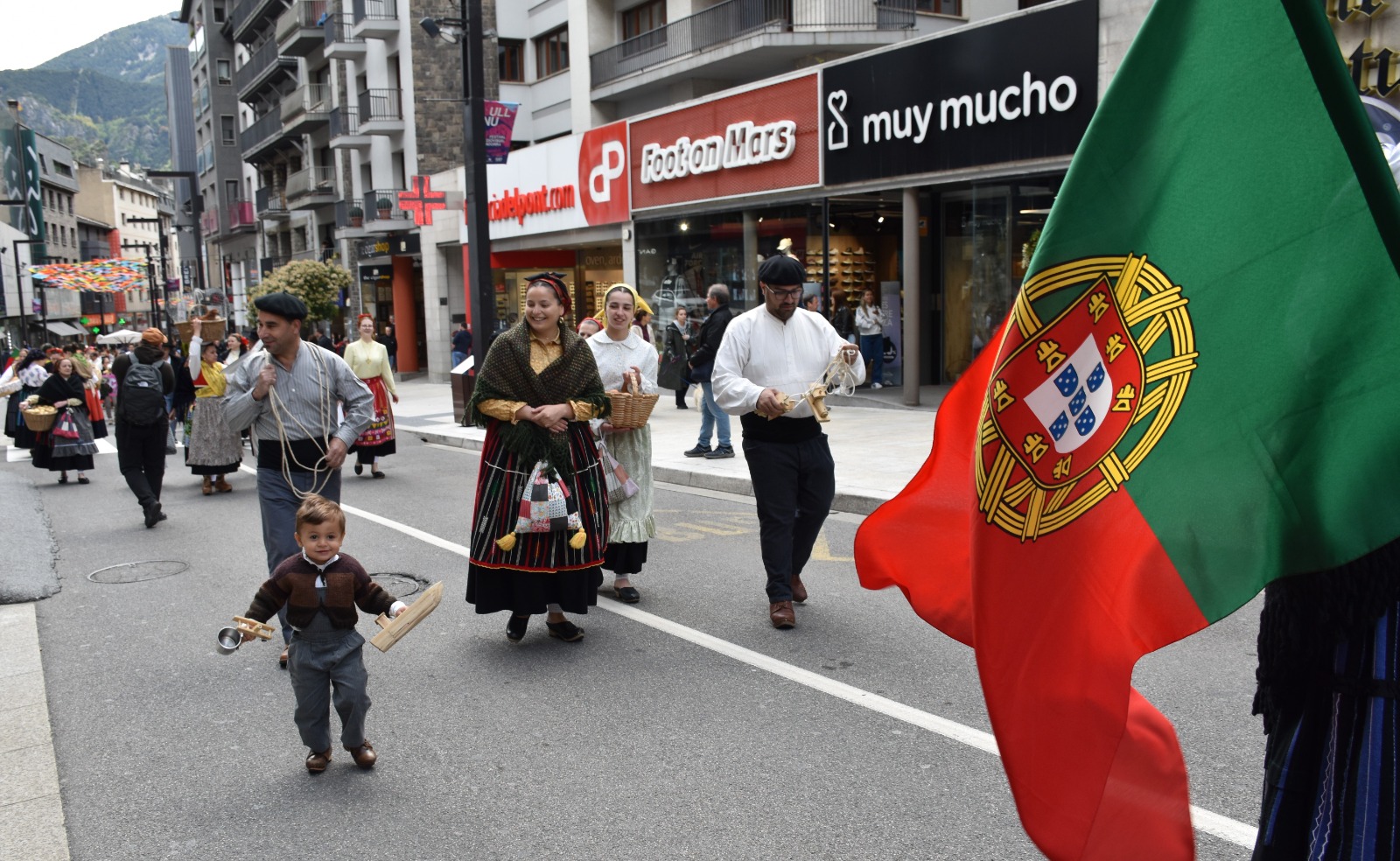 Desfile multicultural nas ruas de Andorra la Vella com pessoas em trajes tradicionais portugueses e uma bandeira de Portugal em destaque, ilustrando a participação da comunidade portuguesa na Semana da Diversidade Cultural.