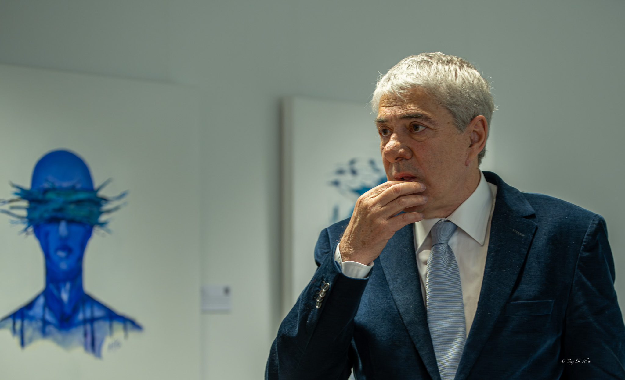 Pessoa de cabelo grisalho, em fato e gravata, sentada num ambiente formal, aparentemente a falar ou ouvir durante uma conferência de imprensa.