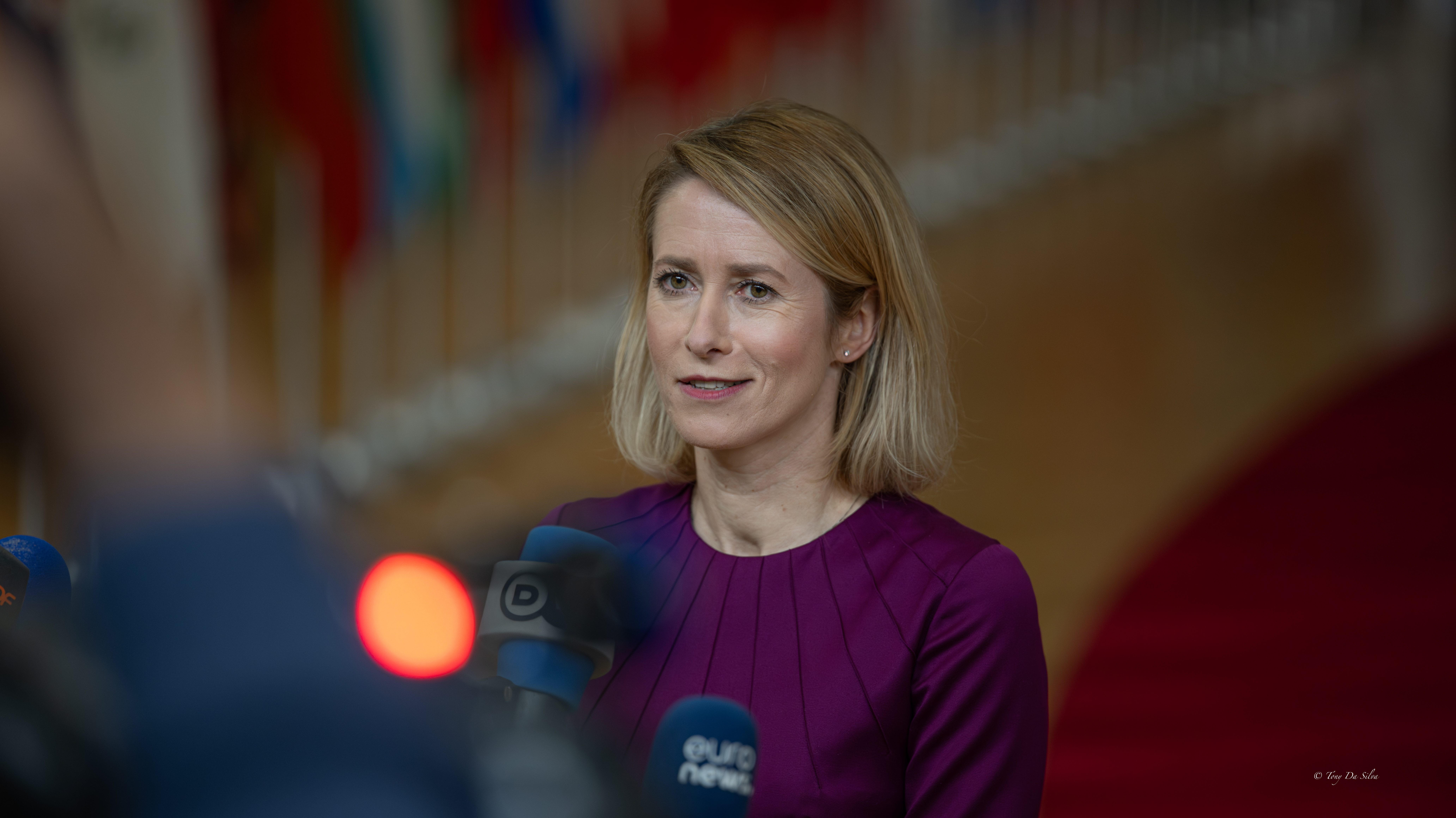 Kaja Kallas, chefe da diplomacia da UE, fala à imprensa com vários microfones à sua frente, num ambiente institucional com bandeiras ao fundo, durante uma reunião em Bruxelas.