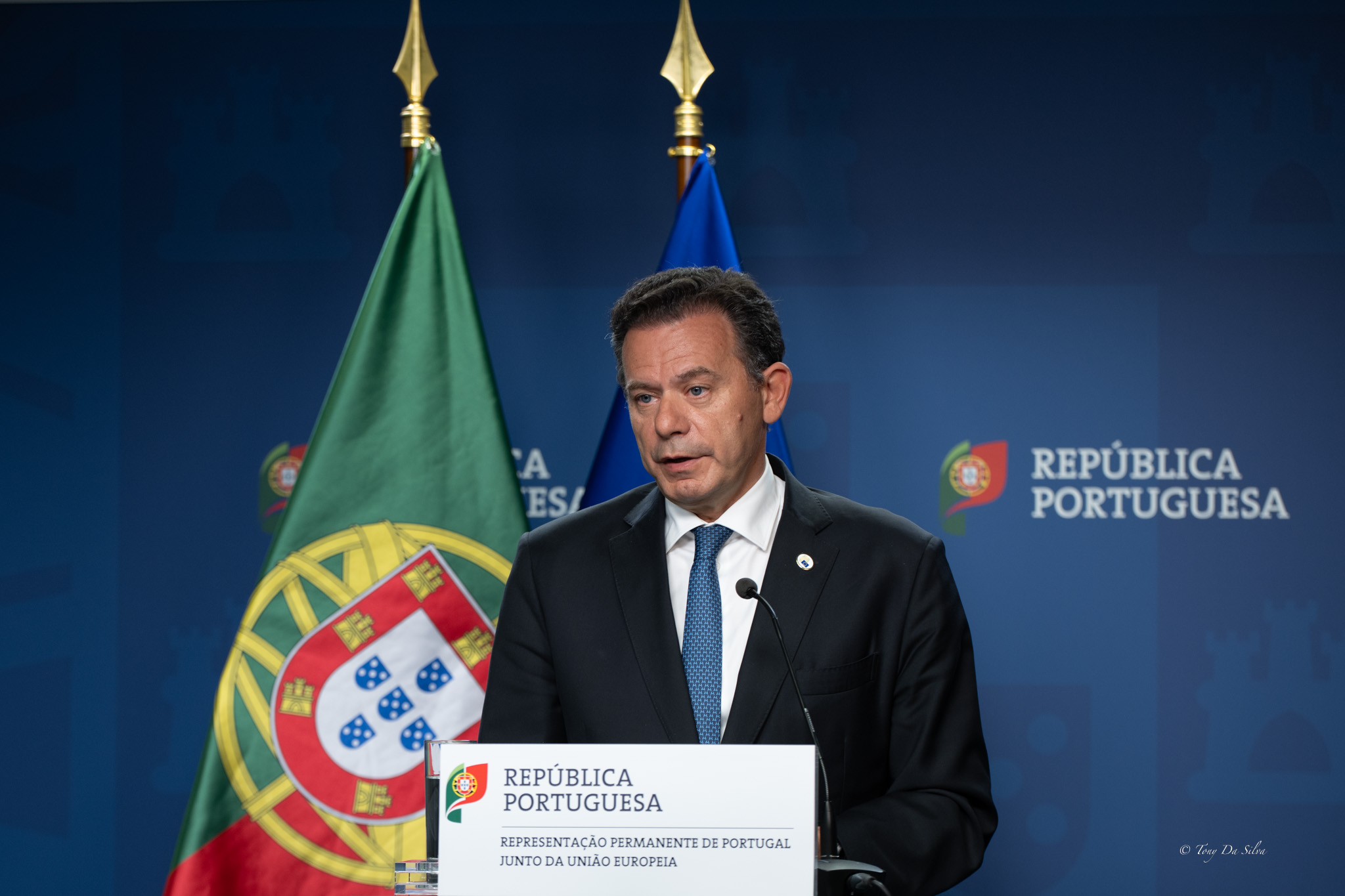 Luís Montenegro, primeiro-ministro português, fala num púlpito oficial com a bandeira de Portugal e o logótipo da República Portuguesa ao fundo, durante uma conferência relacionada com o Conselho Europeu.